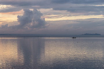 A lake at dusk, with beautiful clouds reflections and a distant fisherman on a little boat