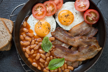 Close-up of english breakfast with fried bacon, eggs, beans in tomato sauce and tomatoes, top view