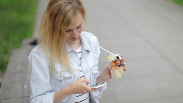 Beautiful Woman Used a Phone and Holds a Cup of Fresh Fruit on the Street