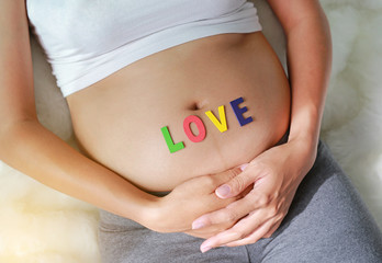 Close up Pregnant woman sitting on soft sofa and touching her belly with sign LOVE in front of her belly.