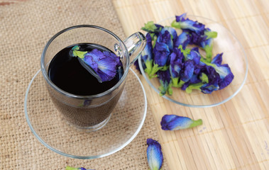 Butterfly pea juice in transparent glass and flowers on sack - wood mat background.