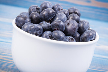 Fresh blueberries in glass bowl on blue boards, natural source of minerals, healthy dessert concept