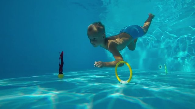 Children's games in the pool.
A little, cute boy sinking in the pool and hunting toys. Underwater shot. Slow motion.
