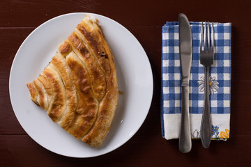 Flat lay above balkan burek pie with cheese and silverware on th