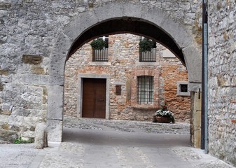 Fototapeta na wymiar Medieval urban background. A stone arch, a stone street and an ancient brick wall house facade in the town of Cividale