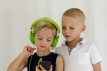 Cute little girl with headphones and cute little boy listening to music on a mobile device