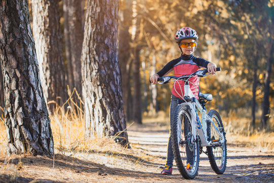 kid on a bicycle in the sunny forest. girl cycling outdoors in helmet