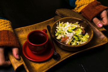 Man holding wooden tray with a salad and coffee on a black background