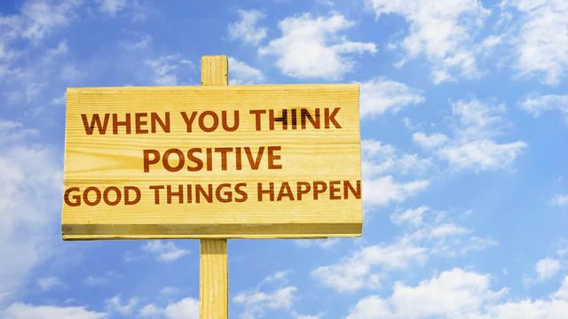 When you think positive good things happen. Words on a wooden sign against time lapse clouds in the blue sky. 