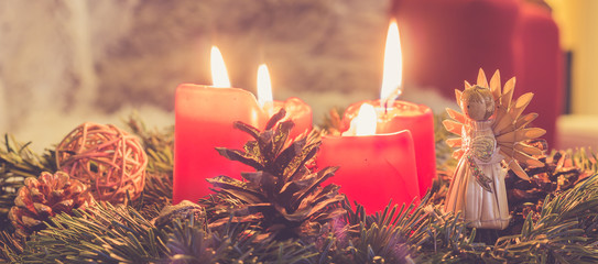Advent wreath Christmas tree sprigs with four burning red candles and a handmade straw angel,...