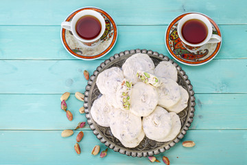 Shot from top. Traditional Iranian and Persian pieces of white nougat dessert sweet candies (Gaz) with Pistachio nuts from Isfahan City and two cups of black tea on blue turquoise wood background