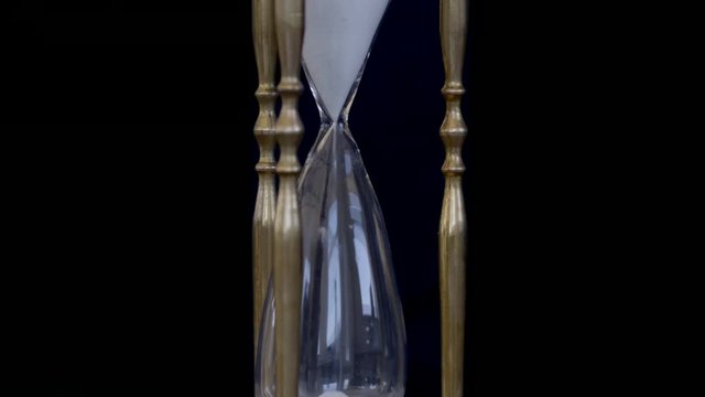 Focus on sand falling through an hour glass with black background. Real time 4K