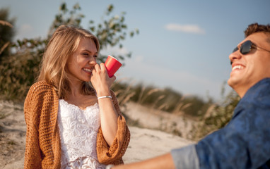 Happy couple sitting at the beach and drinking, love and friendship