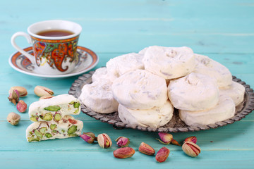 Traditional Iranian and Persian pieces of white nougat dessert sweet candies (Gaz) with Pistachio nuts from Isfahan City and a cup of tea on blue turquoise wood background