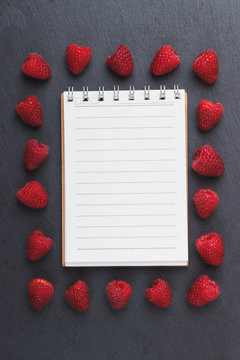 Red raspberries, notebook and a pen on the black slate stone background