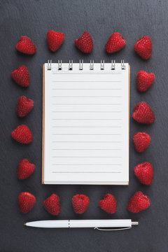 Red raspberries, notebook and a pen on the black slate stone background
