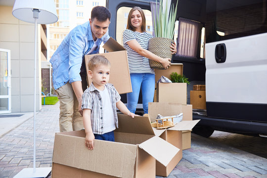 Portrait of happy young family with little son loading cardboard boxes into moving van outdoors