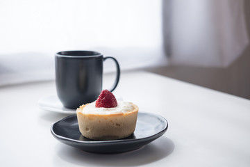 A strawberry cheese tart , a black cup of hot coffee and cactus on white vintage wooden table and curtain background in minimalism cafe