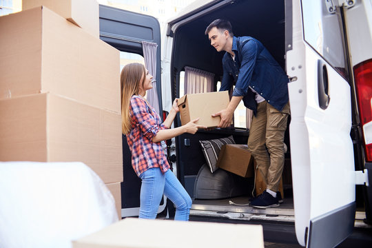 Portrait Of Young  Man Loading Cardboard Boxes To Moving Van With Smiling Wife Helping Him