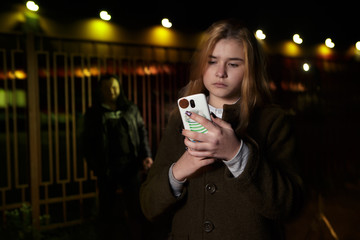 Criminal stalking a girl alone in a dark street. He is hiding in the shadows and the woman is alone...