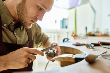 Side view portrait of young jeweler making golden ring in workshop, forming and polishing it on...