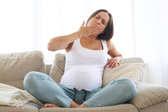 Tired pregnant woman yawning while sitting on sofa
