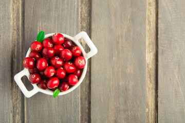 Fresh cranberry in white ceramic bowl on wooden background