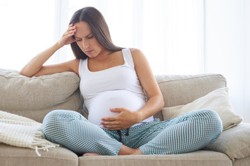 Upset pregnant woman having headache touching her belly