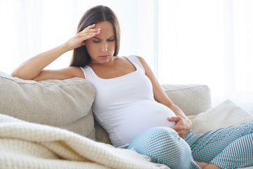 Disappointed pregnant woman sitting on sofa with hand on belly