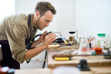Side view portrait of  young man welding metal ring using gas torch in workshop