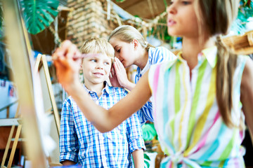 Children discussing gifted little girl in art class, whispering gossips watching her paint pictures on easel