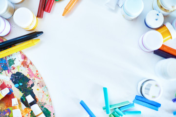 Background image of kids art supplies: colorful pencils, crayons, pastels and palette, scattered...