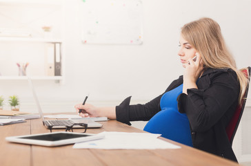 Fototapeta na wymiar Pregnant business lady at work talking on phone