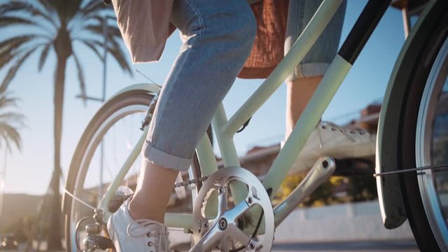 Beautiful summertime mood shot of young woman or girl riding bicycle through beach promenade, in stylish outift, pedalling next to palm trees in sunset light, concept youth and miami