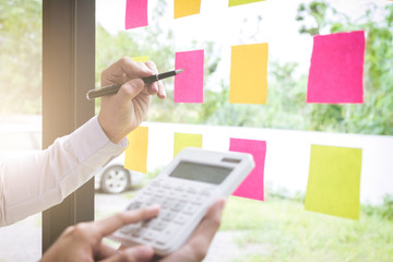 Young creative professional leader using post it notes in glass wall to writing strategy business plan, businesspeople discussing and planning concept