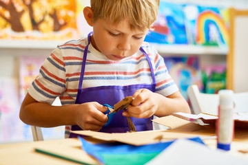 Portrait of cute little boy cutting paper carefully in arts and crafts class of pre-school