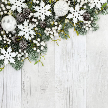 Christmas background border with snowflake and round white bauble decorations, snow covered fir, mistletoe and  pine cones on rustic white wood.
