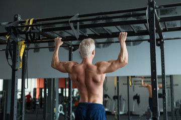Muscular athlete man making Pull-up in gym. Bodybuilder training in fitness club showing his perfect back and shoulder muscles.