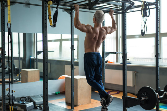 Muscular athlete man making Pull-up in gym. Bodybuilder training in fitness club showing his perfect back and shoulder muscles.