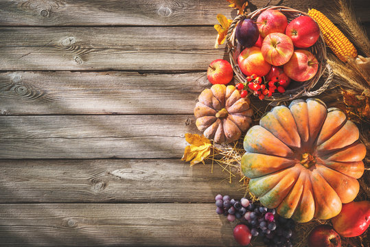 Thanksgiving background with pumpkins and falling leaves on rustic wooden table