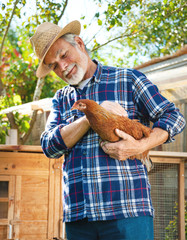 Farmer holds chicken in his arms in front of hen house