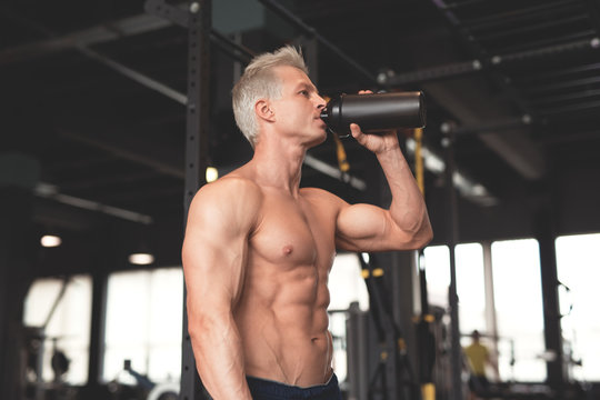 Young muscular man showing his perfect body. Man drinking from a cocktail shaker with the protein. Toned image