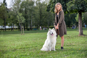 Naklejka na ściany i meble Pretty young girl with her samoyed dog at the park
