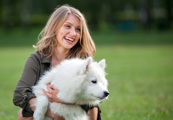 Pretty happy girl playing with her dog at the park, samoyed