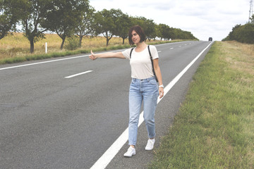 Hitchhiking the road. Female hand gesture,  road trip, travel. Young woman with a backpack hitch-hiking on a road at the fields. concept of people.