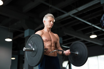 Strong man with muscular body working out in gym. Weight exercise with barbell in fitness club.