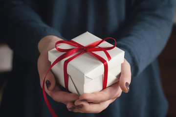 young female hands holding gift box with red ribbon