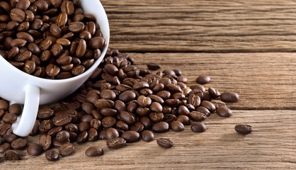 Coffee beans with white cup on wooden table.