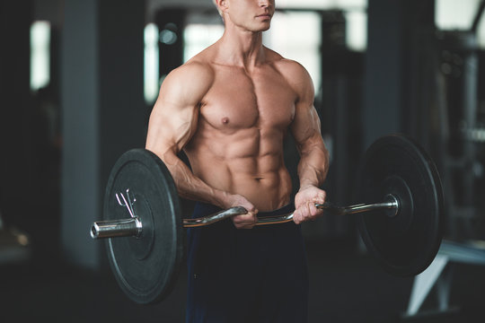 Strong man with muscular body working out in gym. Weight exercise with barbell in fitness club. Toned image