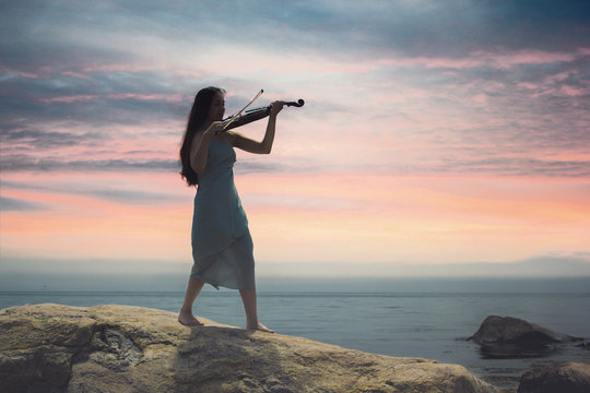 woman playing violin at sunset at the sea